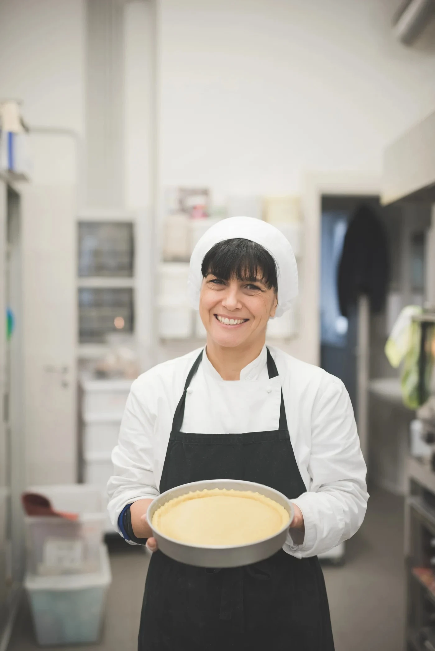 Emily Parker Presenting Tart Crust | CookEaseNow Emily Parker, founder of CookEaseNow, smiling and holding an unbaked tart crust in a professional kitchen.