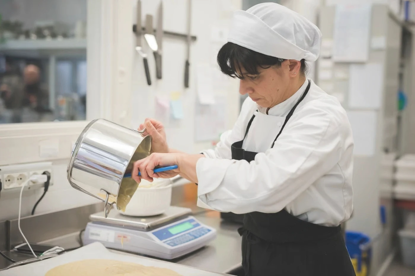 Emily Parker Measuring Ingredients Precisely | CookEaseNow Chef Emily Parker meticulously measuring ingredients by pouring batter onto a kitchen scale for a CookEaseNow recipe.